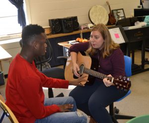 a woman sitting in a chair playing a guitar next to a man.