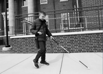 Student walks down the sidewalk with a walking stick