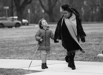 child with cane and adult walk hand in hand