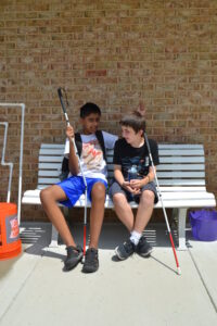Two boys sitting on a bench holding white canes
