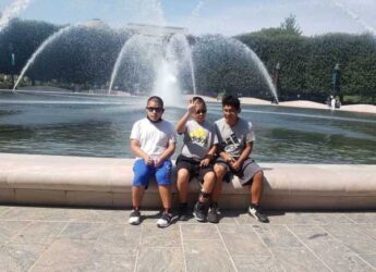 Anderson and his brothers sit on the edge of a large fountain with water spurting behind them.
