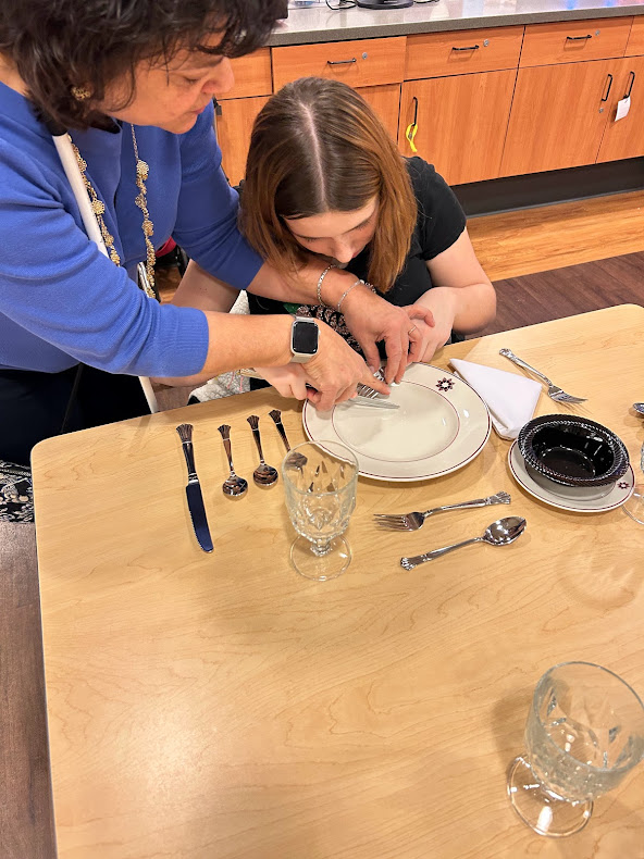 A teacher  models fork and knife cutting strategies for a student.