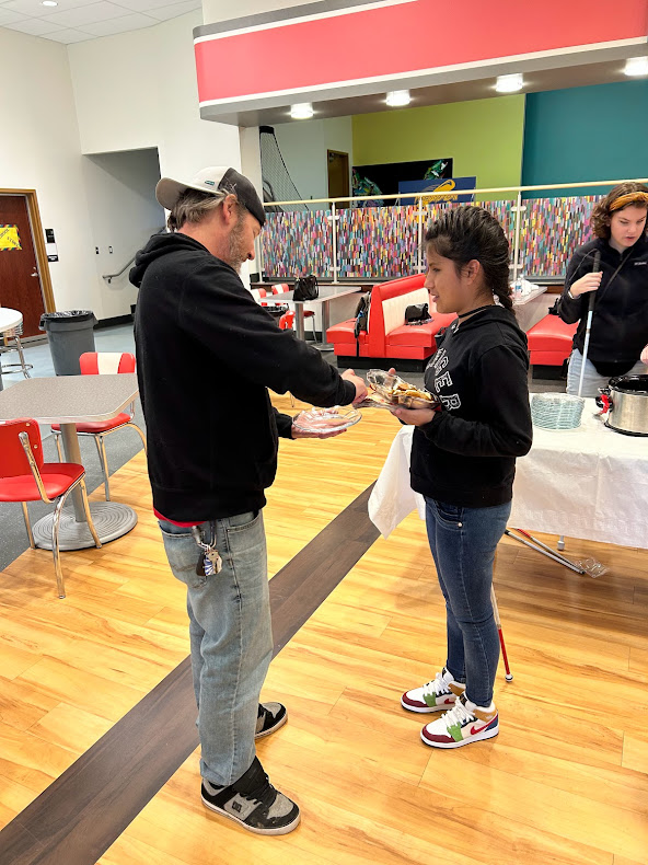 A student greets a reception guest and offers a pumpkin bar and napkin.