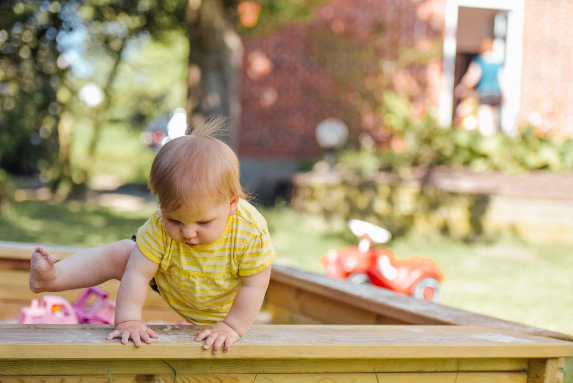 Toddler climbing out of sandbox.