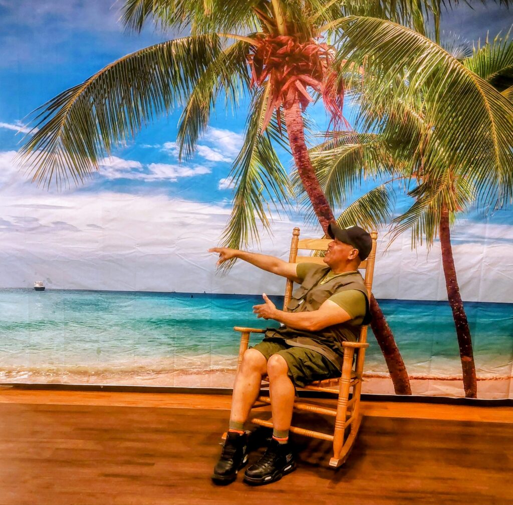 A man sitting in a rocking chair in front of a palm tree.