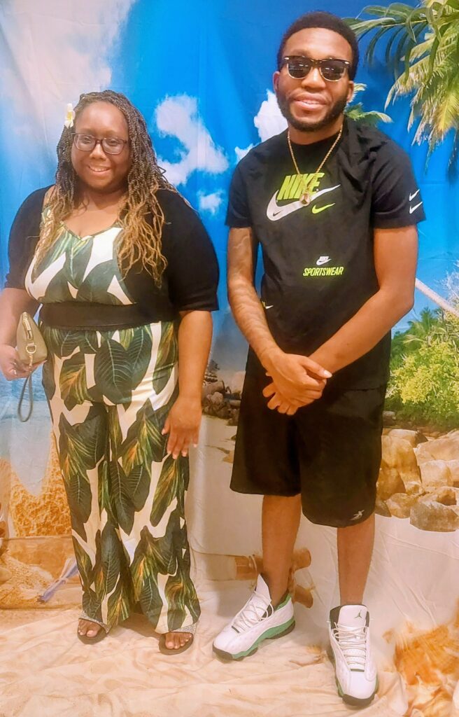Two people posing for a photo in front of a tropical background.