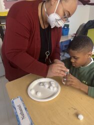 A woman wearing a mask is helping a boy with a plate.