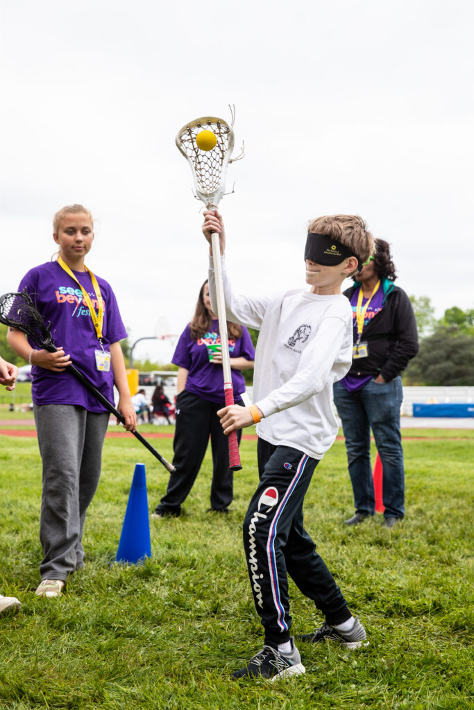 A boy participating in a free lacrosse festival while holding a lacrosse stick.