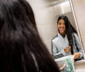 Virginia looks into a mirror as she brushes her hair and smiles.