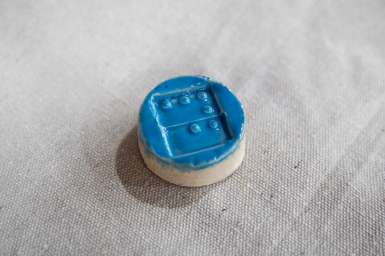 A glazed blue tactile tile with raised Braille dots sits on display.