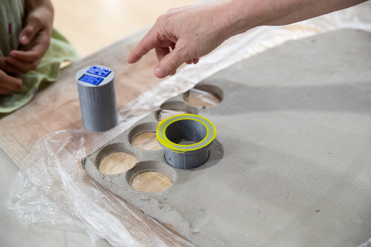 A participant prepares to create a tile, positioning a mold and selecting a Braille stamp.