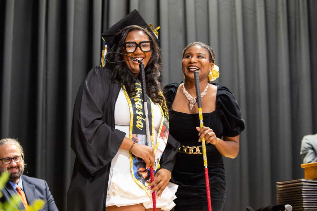 At The Maryland School for the Blind, we celebrate achievement and independence! In this joyful moment captured on stage at our graduation ceremony, two women beam with pride, holding their white canes. One is adorned in a cap, gown, and sashâour newest graduateâwhile another stands beside her in a classic black dress. Behind them, a staff member looks on with a proud smile. This scene beautifully reflects our vibrant community spirit and would make an inspiring cover for the 2025 Summer newsletter!.