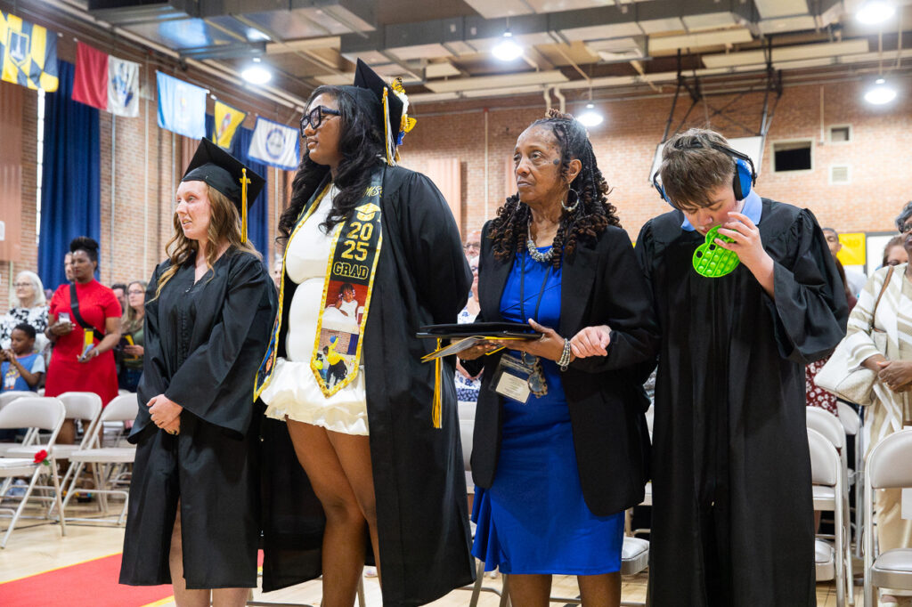 At The Maryland School for the Blind, graduation is a time of joy and accomplishment. In this moment captured for our 2025 Summer Newsletter, four members of our community stand proudly in a row at the ceremony. Two of our graduates are dressed in caps and gowns, symbols of their hard-earned achievements. One wears a bright yellow dress adorned with a sash, while another celebrates by holding up their diploma. Adding to the festive spirit, one graduate playfully blows bubbles as friends and families look on. Behind them, rows of chairs and colorful flags set the stage for this memorable occasionâa testament to the perseverance and success of every MSB student.