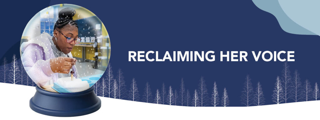 A young woman works on a project inside a snow globe, with the text “Reclaiming Her Voice” next to it on a blue winter-themed background with tree silhouettes.