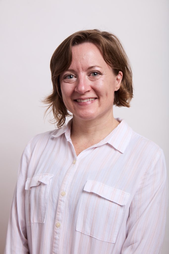 Smiling woman with short brown hair wearing a light button-up shirt against a plain background.