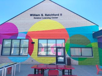 Colorful mural-covered building labeled "William S. Ratchford II Outdoor Learning Center" with outdoor seating and learning spaces at the Maryland School for the Blind.