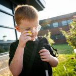 A young boy wearing glasses and holding a flower to his face.