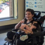 A student smiling and sitting cross-legged in her wheelchair.