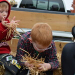 Two boys sitting on hay bales in a trailer behind a pickup truck.