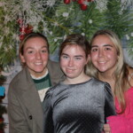 Three girls posing for a picture in front of a christmas tree.
