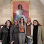Five women standing in front of a painting of Michelle Obama.