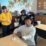 Students engaged in a hands-on activity with clay in a classroom adorned with international flags.