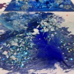 A vibrant mixed-media art piece featuring blue paint, glitter, and textured embellishments on canvas.